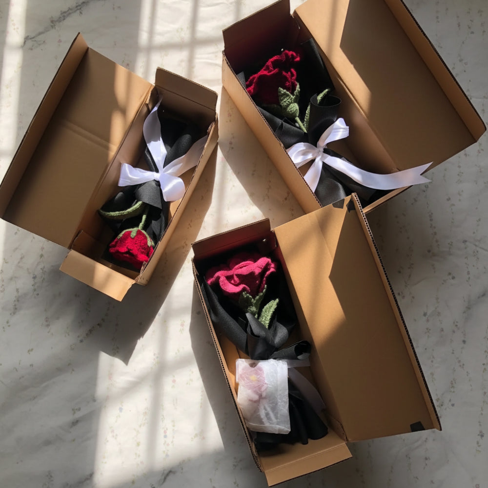 Three cardboard boxes containing red roses with white ribbons on a textured surface.